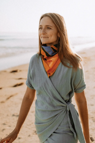 A person on a beach wearing  the "Warm Swims" bandana around their neck.
